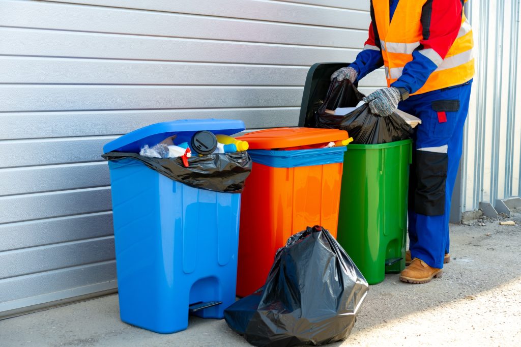 Janitor takes garbage out of trash container outdoors